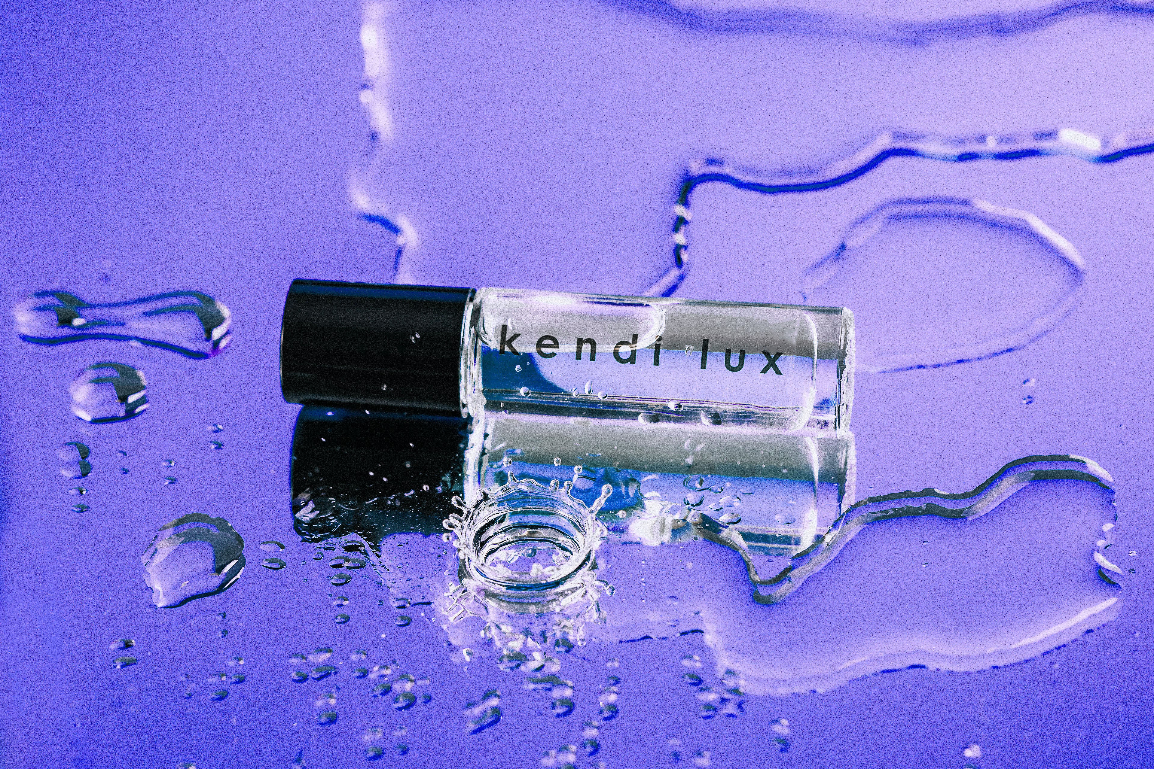 Roll-on bottle of 'kendi lux' on a purple background with water droplets.
